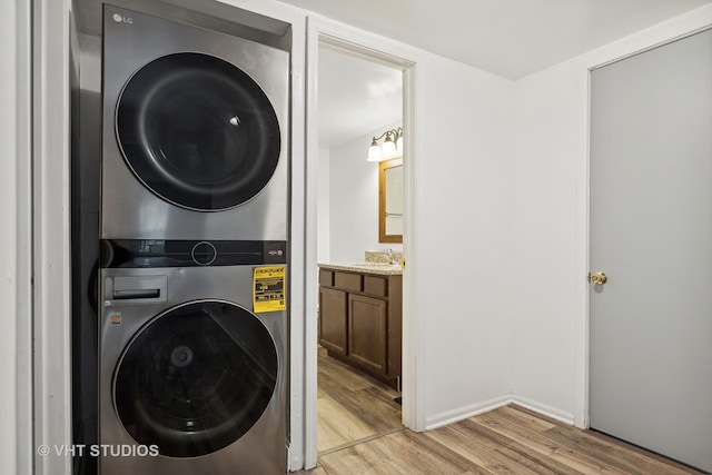 clothes washing area with light wood-type flooring, an inviting chandelier, stacked washer and clothes dryer, and sink