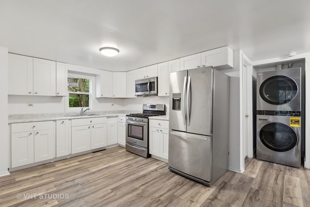 kitchen featuring light hardwood / wood-style floors, white cabinetry, stacked washing maching and dryer, and appliances with stainless steel finishes