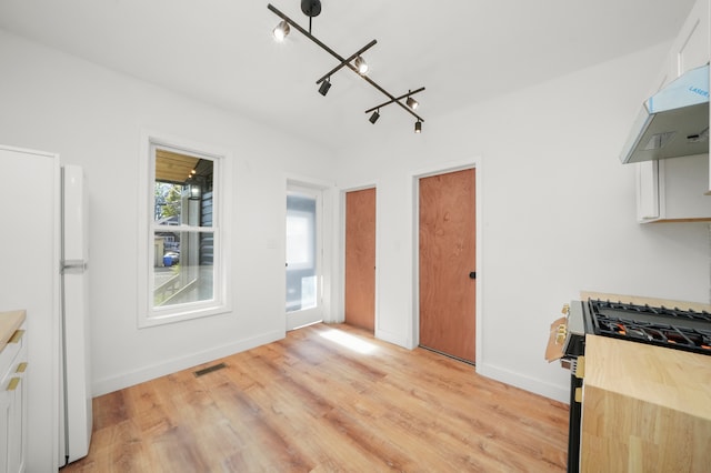 kitchen featuring white cabinetry, stainless steel gas stove, white fridge, and light hardwood / wood-style flooring