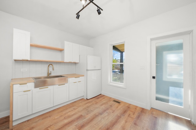 kitchen featuring white fridge, sink, decorative backsplash, white cabinets, and light hardwood / wood-style flooring