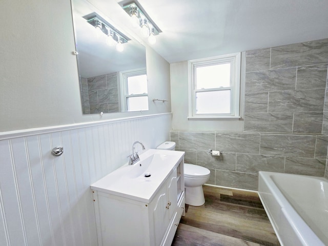 bathroom with toilet, a tub, tile walls, hardwood / wood-style flooring, and vanity