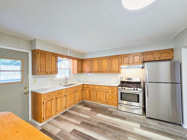 kitchen featuring stainless steel appliances, light hardwood / wood-style floors, sink, and backsplash