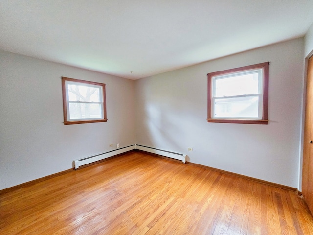 spare room featuring a healthy amount of sunlight, light hardwood / wood-style flooring, and a baseboard heating unit