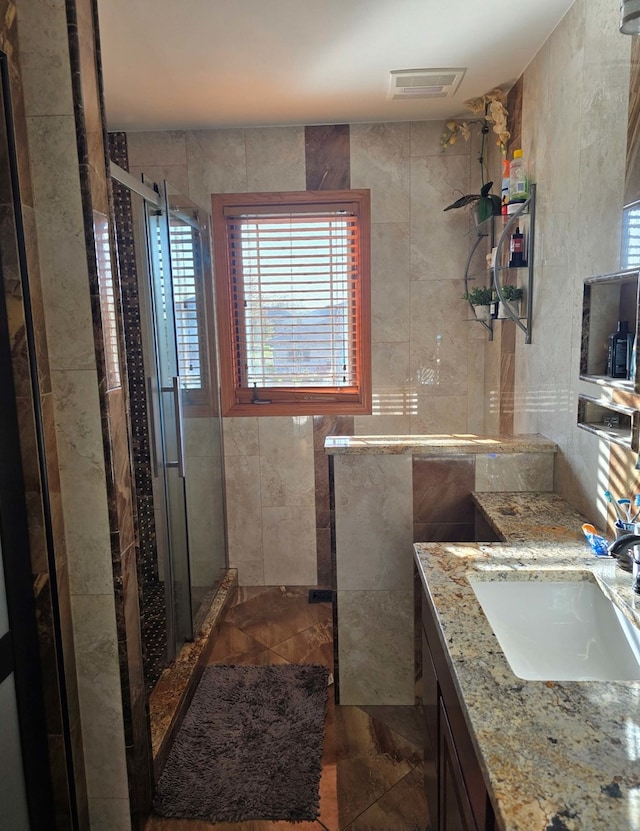 full bathroom with a stall shower, visible vents, tile walls, and vanity