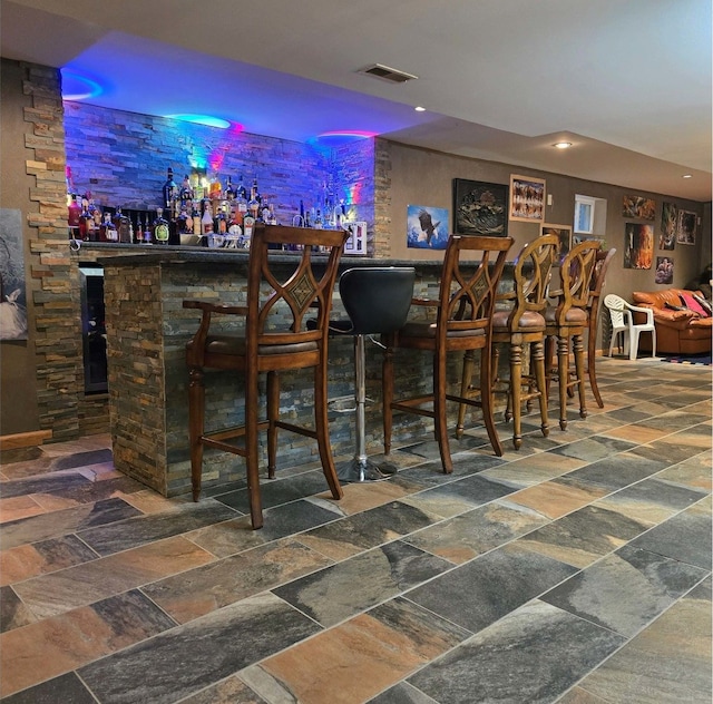 bar featuring visible vents, stone tile floors, and a bar