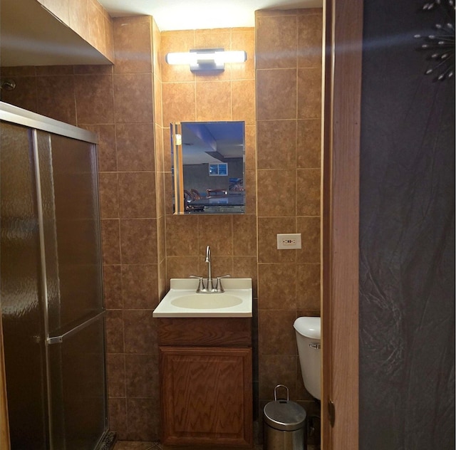 bathroom with toilet, a shower stall, tile walls, and vanity