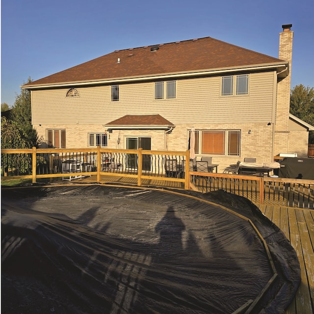 back of house with brick siding, a chimney, and a wooden deck