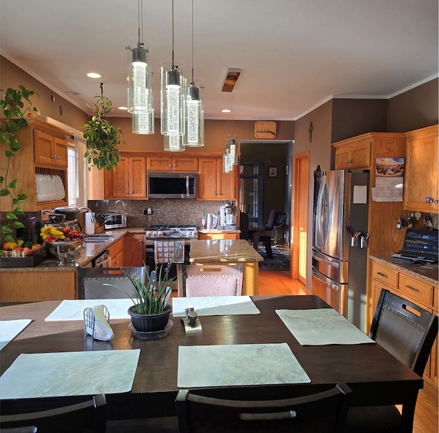 kitchen featuring light stone counters, stainless steel appliances, hanging light fixtures, brown cabinets, and tasteful backsplash