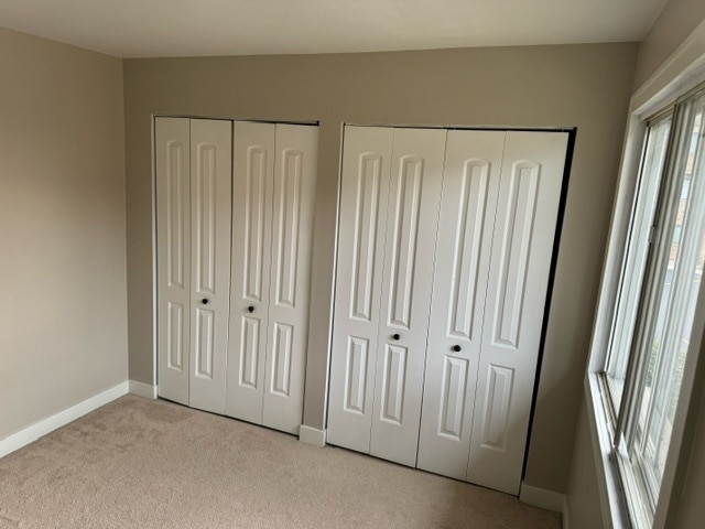 unfurnished bedroom with light carpet and two closets