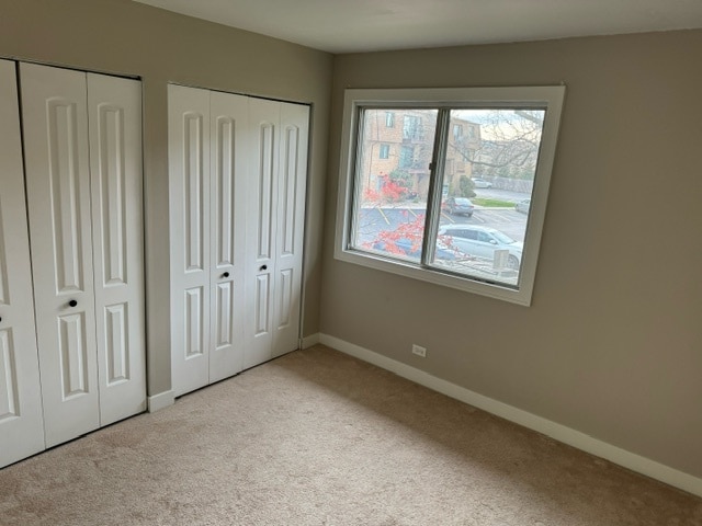 unfurnished bedroom featuring light colored carpet and two closets