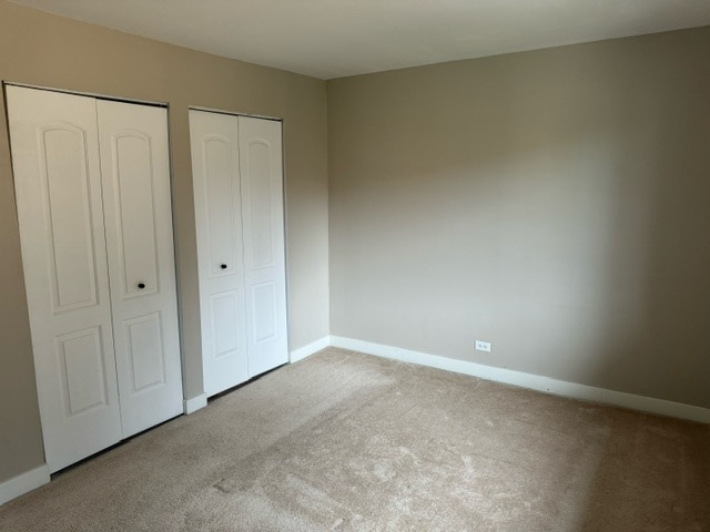 unfurnished bedroom with multiple closets and light colored carpet