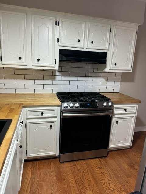 kitchen with stainless steel range with gas cooktop, wooden counters, hardwood / wood-style floors, white cabinets, and decorative backsplash