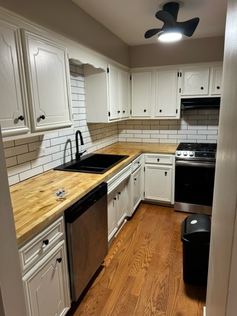 kitchen with stainless steel appliances, wood counters, sink, white cabinets, and light hardwood / wood-style flooring