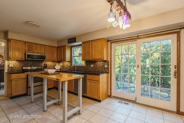 kitchen with stainless steel appliances, light tile patterned flooring, a healthy amount of sunlight, and decorative backsplash