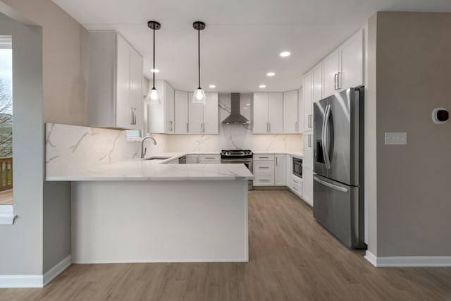 kitchen featuring kitchen peninsula, appliances with stainless steel finishes, wall chimney exhaust hood, decorative light fixtures, and white cabinets