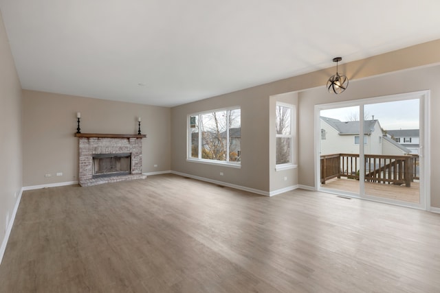 unfurnished living room with a fireplace, an inviting chandelier, and light hardwood / wood-style flooring