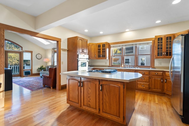 kitchen with lofted ceiling, sink, light hardwood / wood-style floors, appliances with stainless steel finishes, and a kitchen island