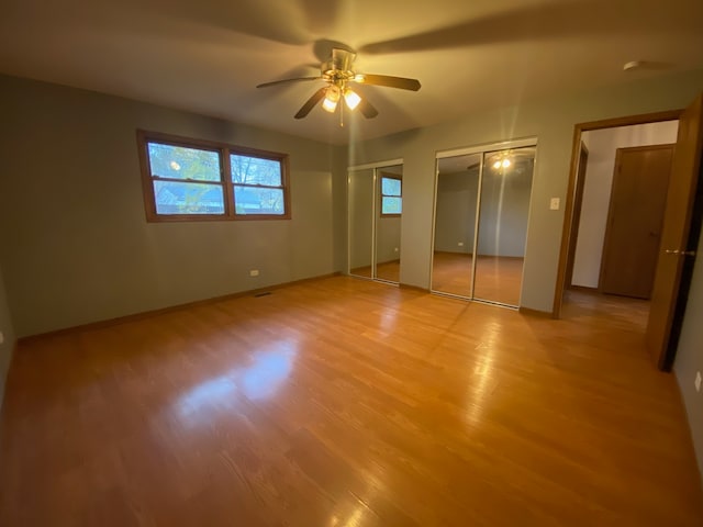 unfurnished bedroom featuring two closets, light hardwood / wood-style floors, and ceiling fan