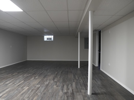 basement featuring dark hardwood / wood-style floors, a drop ceiling, and electric panel