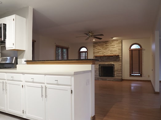 kitchen featuring white cabinetry, ceiling fan, dark hardwood / wood-style flooring, kitchen peninsula, and a fireplace