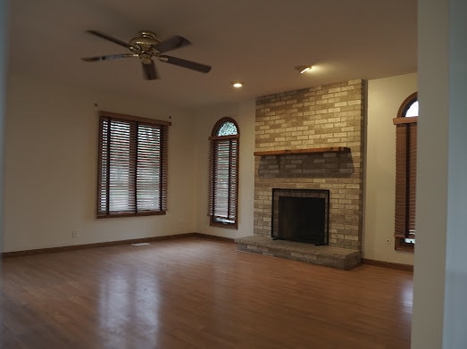 unfurnished living room featuring ceiling fan, wood-type flooring, and a fireplace