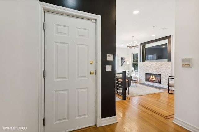 entrance foyer with a stone fireplace, a chandelier, and wood-type flooring