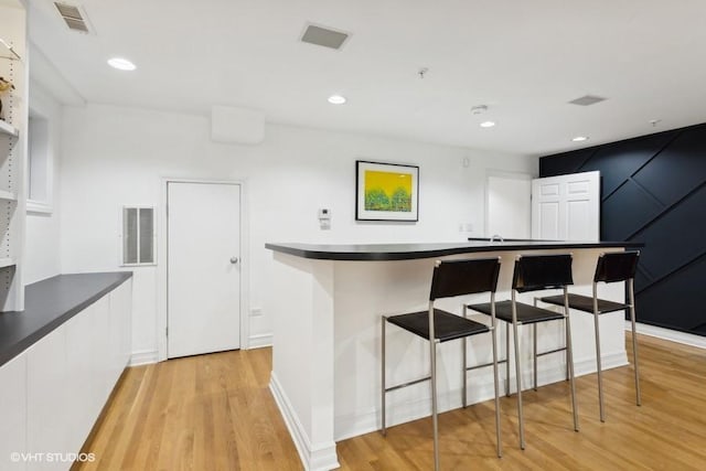 kitchen featuring a breakfast bar area, white cabinets, and light wood-type flooring