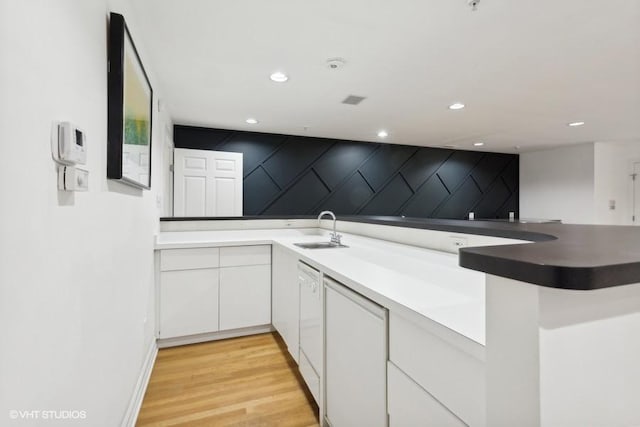 kitchen featuring white cabinetry, sink, kitchen peninsula, white dishwasher, and light hardwood / wood-style floors