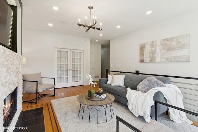 living room with a stone fireplace, hardwood / wood-style floors, a chandelier, and french doors