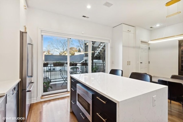 kitchen with hanging light fixtures, light hardwood / wood-style flooring, appliances with stainless steel finishes, a kitchen island, and white cabinetry