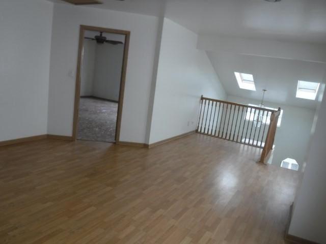 unfurnished room featuring hardwood / wood-style floors, ceiling fan, and lofted ceiling with skylight