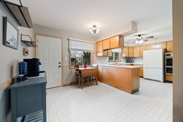 kitchen with kitchen peninsula, stainless steel double oven, ceiling fan with notable chandelier, sink, and white refrigerator