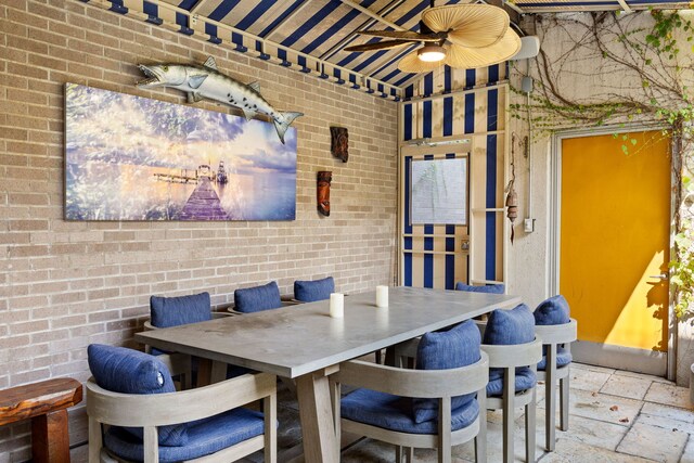 dining area featuring ceiling fan and brick wall