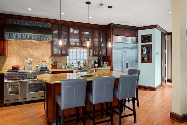 bar featuring light hardwood / wood-style floors, premium appliances, hanging light fixtures, ventilation hood, and light stone countertops