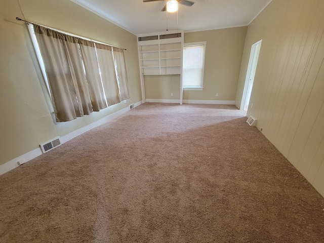 carpeted empty room featuring built in features, wood walls, ornamental molding, and ceiling fan