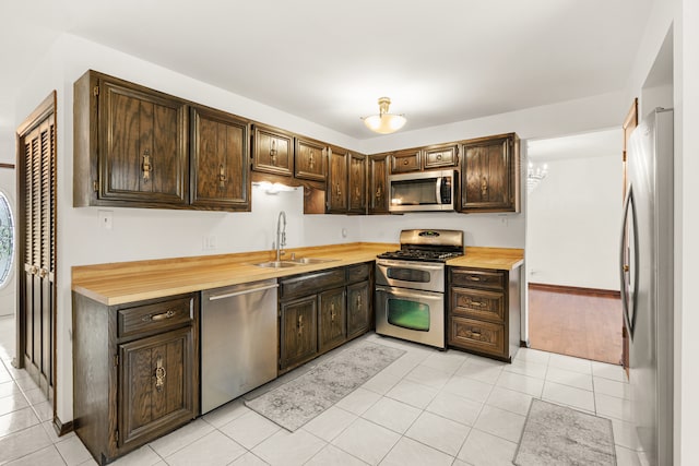 kitchen with dark brown cabinetry, sink, light tile patterned flooring, and stainless steel appliances