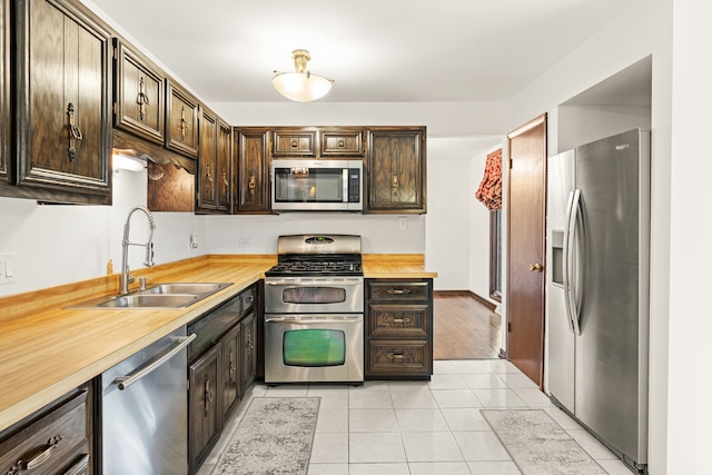 kitchen featuring wooden counters, appliances with stainless steel finishes, dark brown cabinetry, sink, and light tile patterned floors