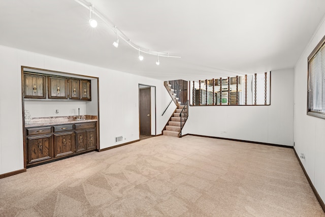 unfurnished living room featuring light carpet, track lighting, and indoor wet bar