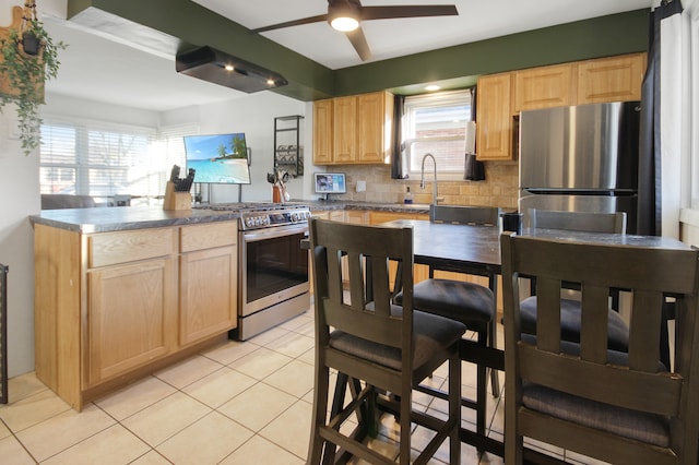 kitchen with light brown cabinetry, decorative backsplash, stainless steel stove, and a wealth of natural light