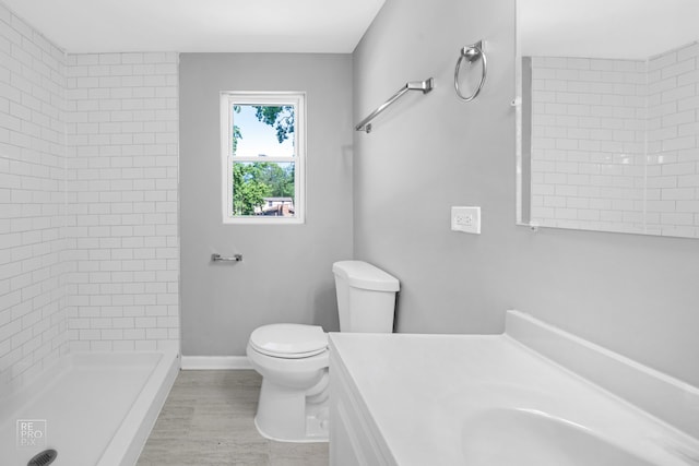 bathroom with a tile shower, vanity, hardwood / wood-style flooring, and toilet