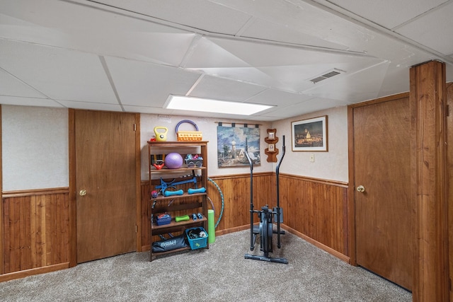 workout area with carpet flooring, a paneled ceiling, and wood walls