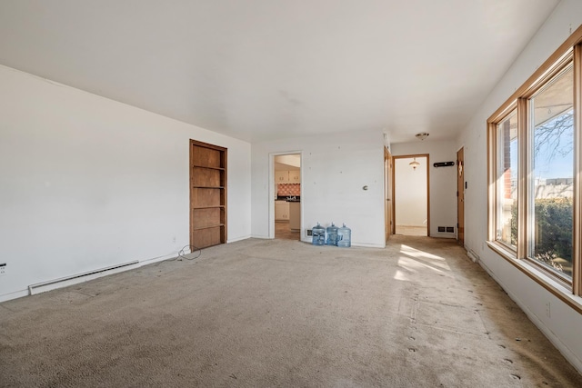 unfurnished living room with light colored carpet, baseboard heating, and built in shelves