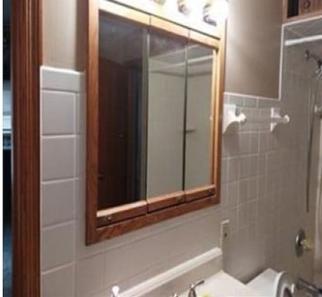 bathroom with tiled shower / bath, toilet, and tile walls