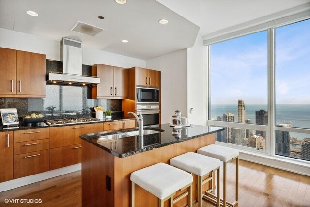 kitchen featuring wall chimney exhaust hood, a kitchen bar, decorative backsplash, and stainless steel appliances