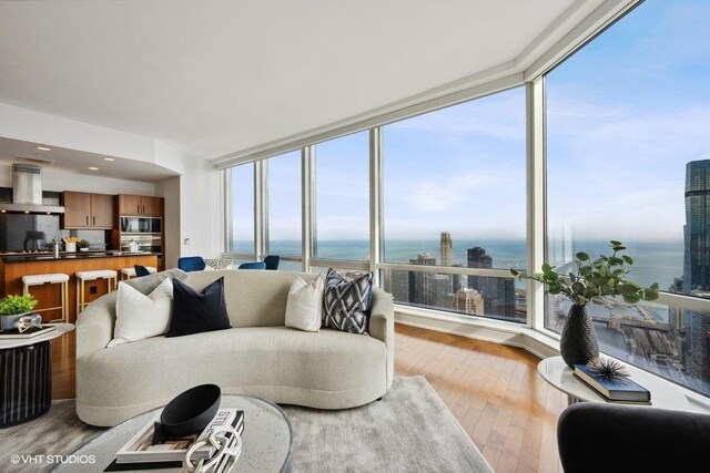 living room with light wood-type flooring, a water view, and expansive windows