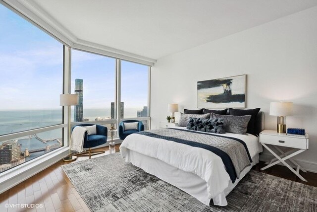 bedroom with expansive windows, hardwood / wood-style floors, and a water view