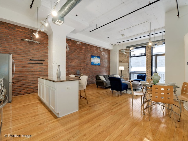 kitchen featuring white cabinetry, light wood-type flooring, stainless steel refrigerator, dark stone countertops, and brick wall