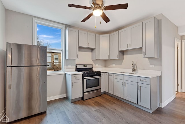 kitchen with gray cabinetry, ceiling fan, sink, stainless steel appliances, and light wood-type flooring