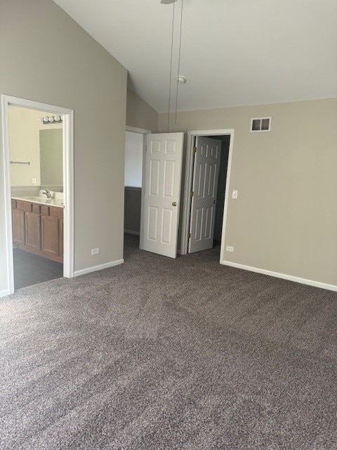 unfurnished bedroom with a closet, dark carpet, connected bathroom, sink, and vaulted ceiling