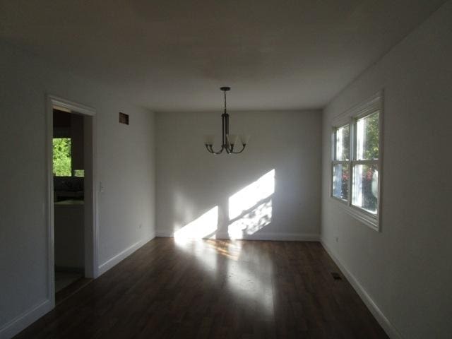 unfurnished dining area featuring dark hardwood / wood-style flooring, a wealth of natural light, and a chandelier